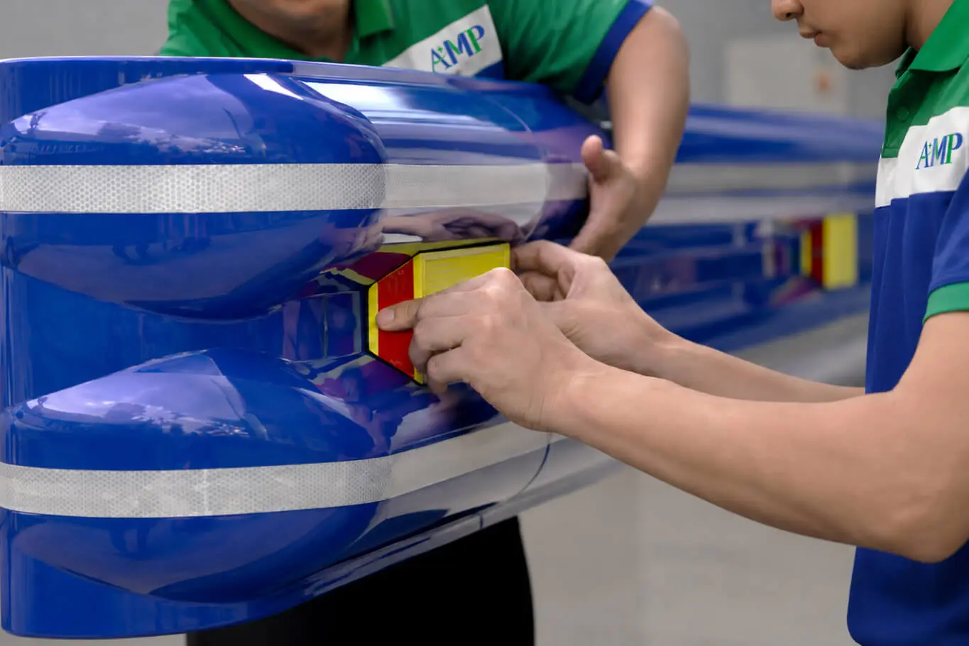 AMP technicians installing a yellow and red directional reflector on a blue ASP polycarbonate highway guardrail