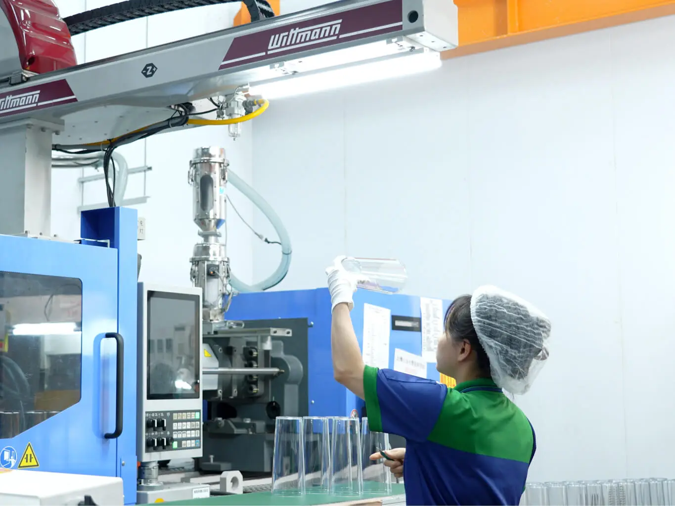 AMP technician inspecting clear plastic containers beside Wittmann production equipment in a clean manufacturing area
