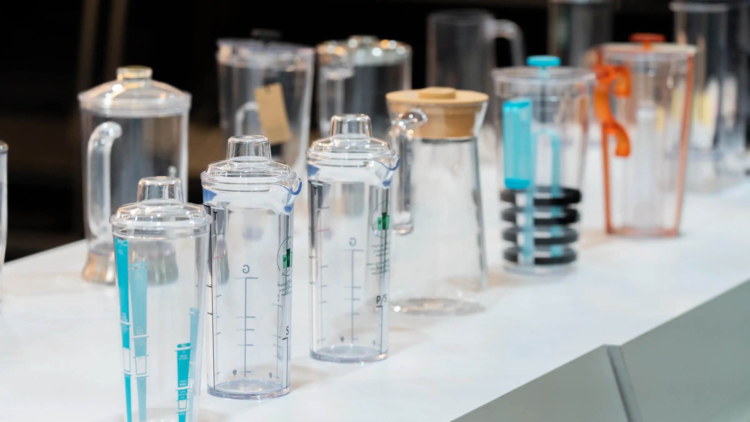 Clear injection-molded plastic beverage containers with measurement markings, manufactured by AMP