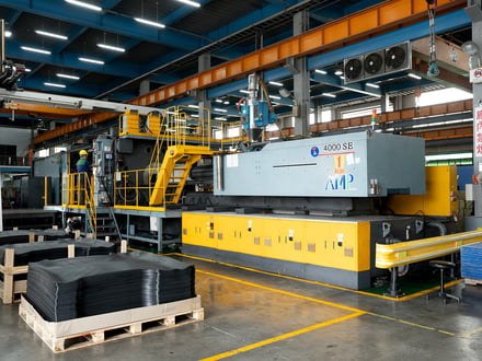 AMP's 4000 SE large-tonnage injection molding machine with palletized automotive floor mats in the foreground, running 24-hour production