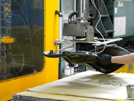 AMP robotic extraction removing a molded seat panel from the injection molding press, with operator guiding the part to staging