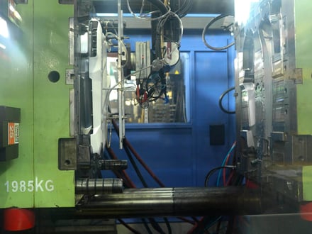 AMP injection molding machine with a 1,985 kg mold installed and open between the platens, showing cavity and core sides with cooling and hydraulic connections