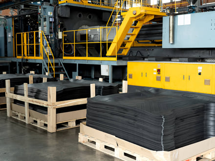 AMP palletized automotive floor mats stacked beside our large-tonnage press, produced in high-volume serial runs on 24-hour production schedules