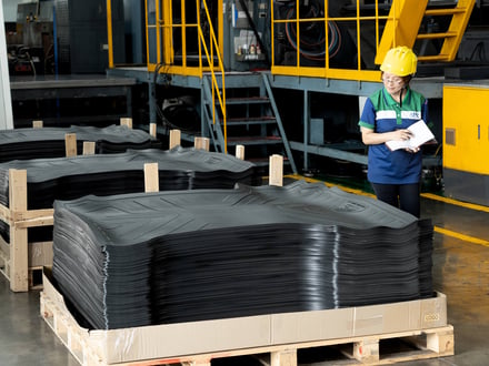 AMP quality team member reviewing production records alongside palletized injection-molded automotive floor mats staged for shipment