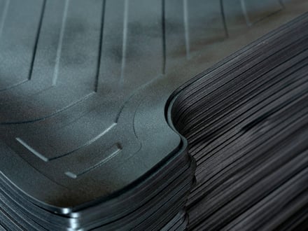 AMP injection-molded automotive floor mats showing consistent edge definition, raised lip profile, and surface texture across stacked production parts