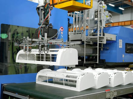 AMP robotic arm extracting an appliance housing from the injection molding machine, with finished parts staged on the conveyor for secondary operations