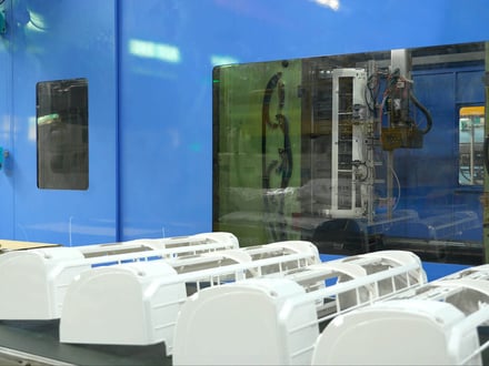 AMP injection-molded appliance housings staged beside the press, with the mold and robotic extraction system visible through the safety guard