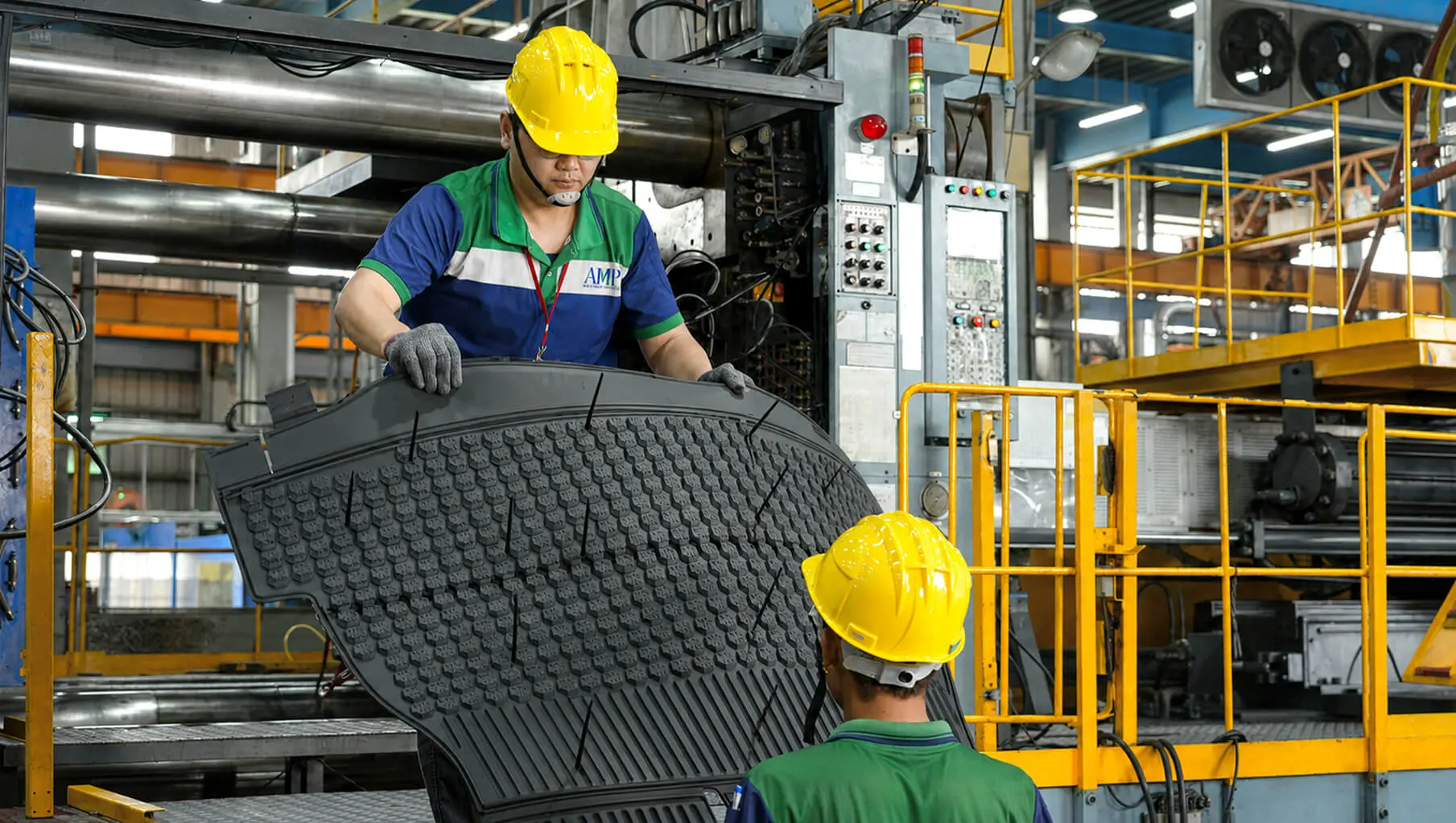 AMP operators handling a large injection-molded automotive floor mat with textured tread pattern, produced on our large-tonnage press fleet