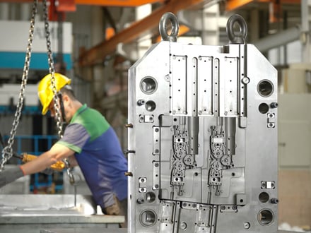 AMP-built multi-cavity injection mold with slide actions, ejector mechanisms, and lifting eyes, positioned by overhead crane on our assembly floor