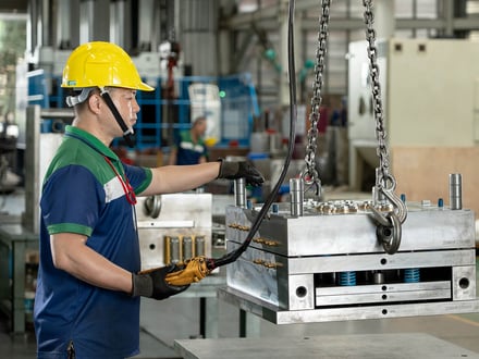AMP toolmaker positioning a fully assembled injection mold with cooling fittings and return springs via overhead crane, moving it to trial on our production machines