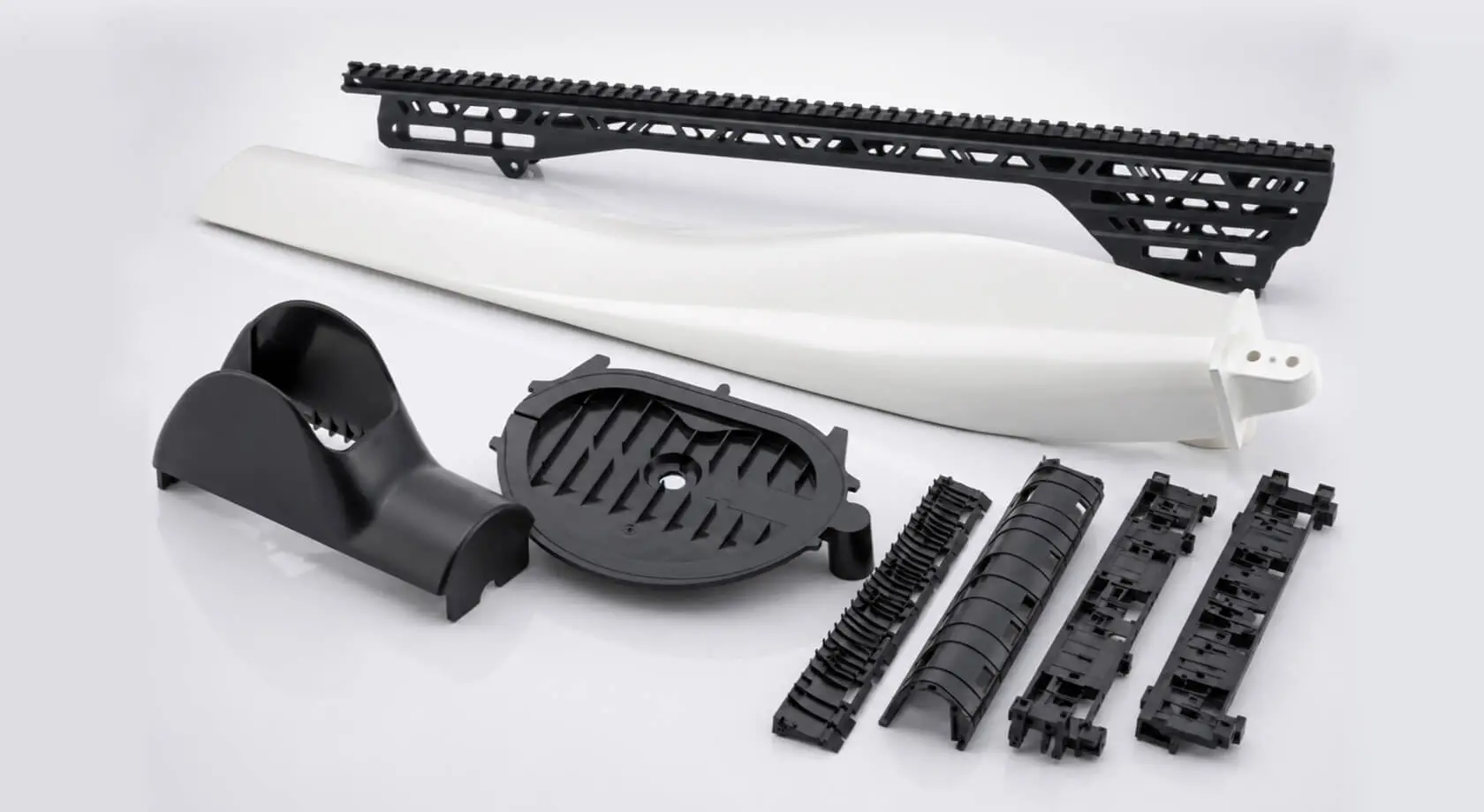 Assortment of injection-molded plastic components for other industries, including a structural rail, wind turbine blade section, housings, and connector parts manufactured by AMP