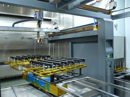 AMP's automated clean room spray painting line with parts fixtured on jigs and conveyed through the paint booth for consistent surface coating in-house
