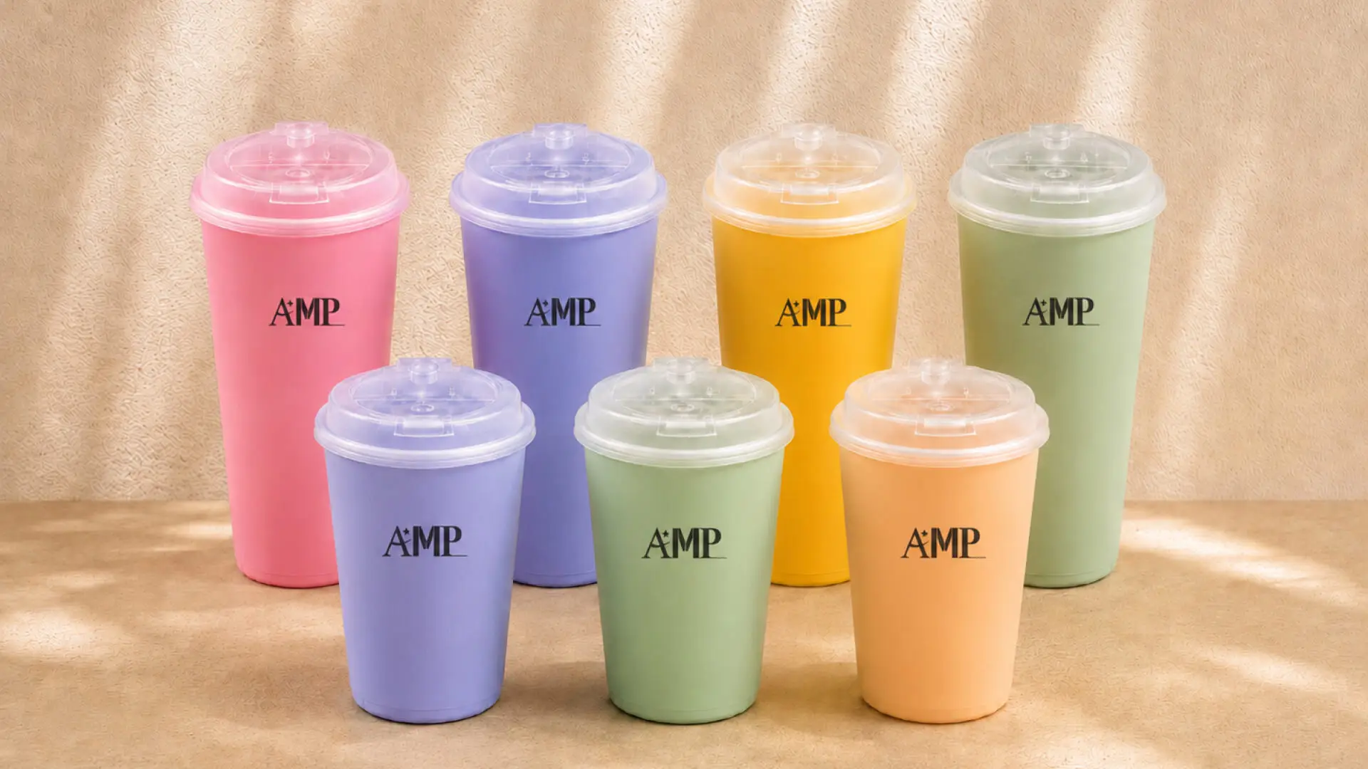 AMP-branded supercritical foam tumblers in pastel colors arranged on a sand-colored surface