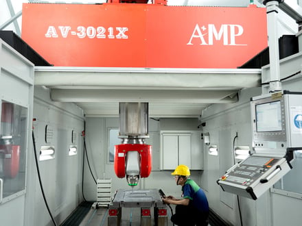 AMP's AV-3021X 5-axis gantry machining center with operator setting up a mold base, handling work up to 3,000 × 2,100 × 1,000 mm in a single setup