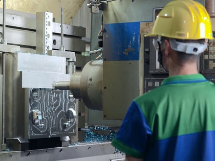 AMP toolmaker monitoring a large mold base during CNC machining, with steel chips visible from heavy cutting on in-house equipment